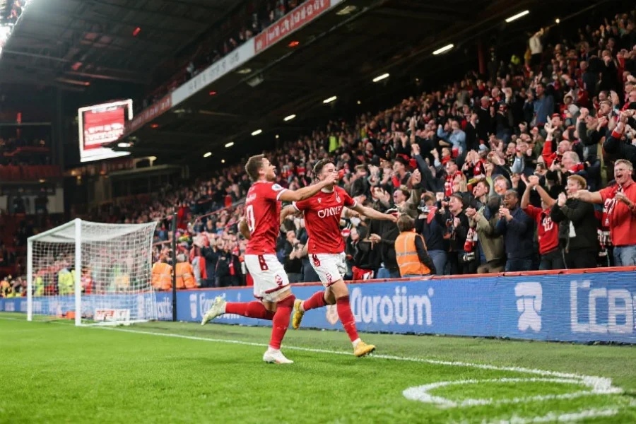 现代足球场景，展示主队球员在主场观众的加油声中庆祝进球