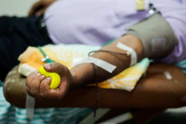 Midsection of a man in violet shirt giving a blood donation, arm is outstretched, hand is squeezing yellow ball
